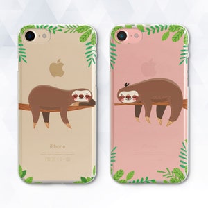 May include: Two clear phone cases with a pink and beige background. Each case features a green leafy design and a cartoon sloth hanging from a branch.