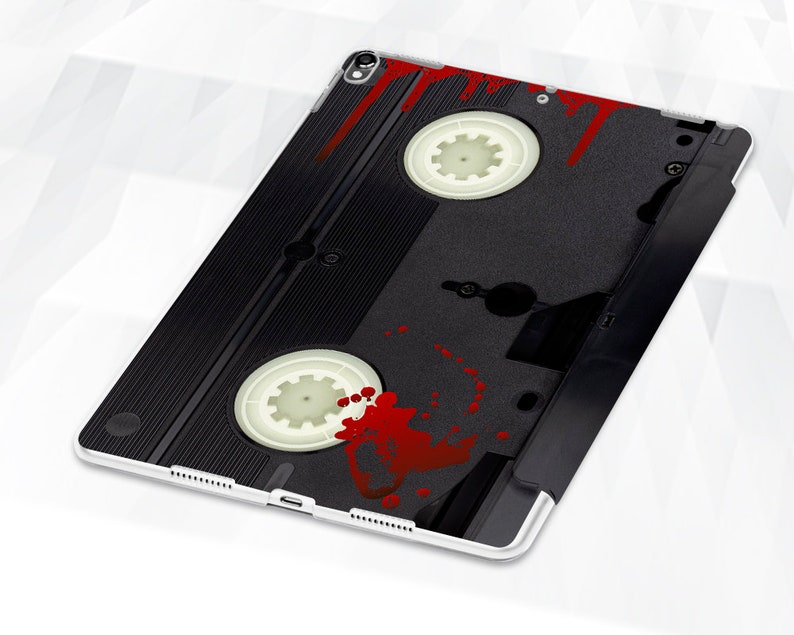 May include: A black and white VHS cassette tape with red blood splatter on the front. The tape is on a white background.