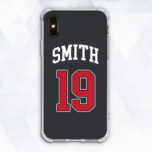 Puede incluir: Una funda de teléfono negra con un diseño blanco y rojo. La funda tiene el nombre "SMITH" y el número "19" impreso en ella.