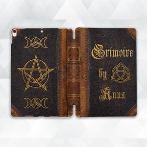 Peut inclure: Étui pour tablette marron foncé avec un design de livre ancien. La couverture présente des symboles dorés en relief, dont un pentagramme, des croissants de lune et le titre "Grimoire by Anna". La tranche est marron avec des détails dorés.