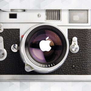 Può includere: Una macchina fotografica in stile vintage con un esterno in pelle nera e un obiettivo in metallo argentato. L'obiettivo ha una grande apertura circolare e un logo Apple bianco al centro.