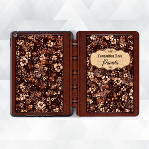 Puede incluir: Una funda de iPad de cuero marrón con un patrón floral y una inscripción dorada que dice "Composition Book Pamela".