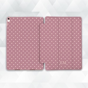 May include: A pink tablet case featuring a white polka dot design. The case is displayed open, showcasing the interior and exterior. The initials "EM" are printed on the cover.