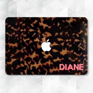 Può includere: Skin per laptop con motivo tartarugato nei toni del marrone e del nero. Un logo Apple bianco è centrato in alto. Il nome "DIANE" è stampato in rosa in basso a destra.