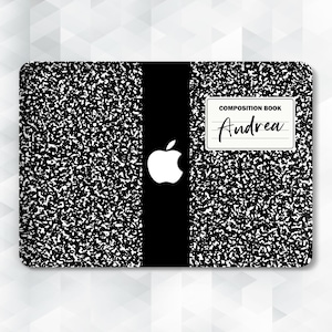 Puede incluir: Piel de portátil negra y blanca con textura de cuaderno de composición, con una franja negra en el centro y un logotipo de Apple. La piel tiene una textura de cuaderno de composición y dice "COMPOSITION BOOK" y "Andrea" en una etiqueta blanca.