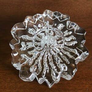 Pu&ograve; includere: Un portacandele in vetro trasparente con un design a stella. Il portacandele ha un centro rialzato per una candela e un bordo smerlato.