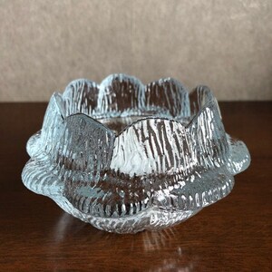 May include: A clear glass bowl with a scalloped edge and a textured surface. The bowl is designed to resemble a flower.