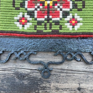 May include: A black metal wall hanging with a decorative design. The hanging has a rectangular top with a textured surface and three curved hooks at the bottom.