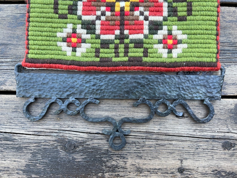 May include: A black metal wall hanging with a decorative design. The hanging has a rectangular top with a textured surface and three curved hooks at the bottom.