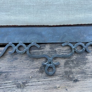 May include: A black metal decorative bracket with a scrolled design. The bracket is attached to a wooden surface.