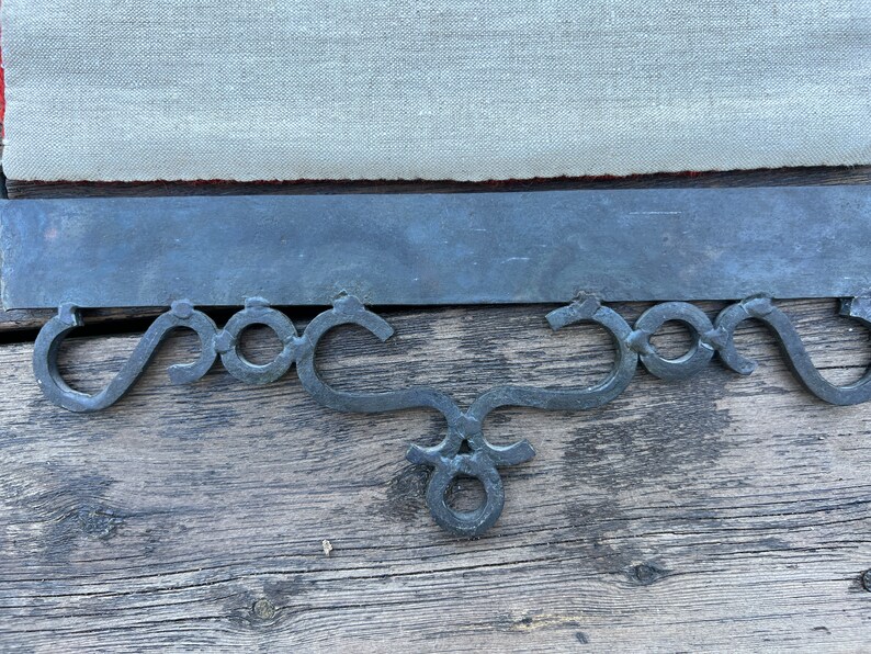 May include: A black metal decorative bracket with a scrolled design. The bracket is attached to a wooden surface.