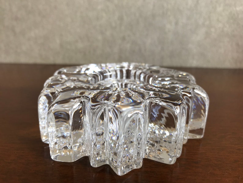 Pu&ograve; includere: Un portacandele in vetro trasparente con un design a forma di stella. Il portacandele ha una superficie testurizzata e un'apertura rotonda al centro.