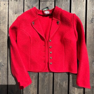 Puede incluir: Una chaqueta de lana roja con cierre de botones y una peque&ntilde;a etiqueta en el cuello. La chaqueta tiene un estilo tradicional con una longitud ligeramente recortada.
