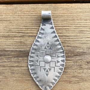 May include: A silver pendant in the shape of a teardrop with a geometric design. The pendant has a loop at the top for attaching a chain.