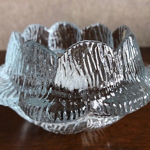 May include: A clear glass candle holder with a textured, rippled surface. The holder has a rounded, flower-like shape with multiple points.