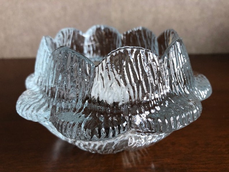 May include: A clear glass candle holder with a textured, rippled surface. The holder has a rounded, flower-like shape with multiple points.