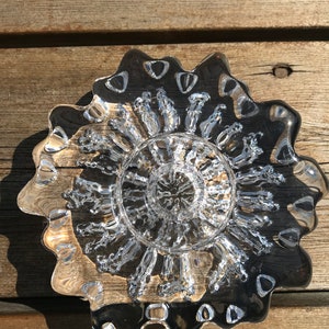 Pu&ograve; includere: Un piatto di vetro trasparente con un bordo ondulato e un design testurizzato a forma di bolle al centro.