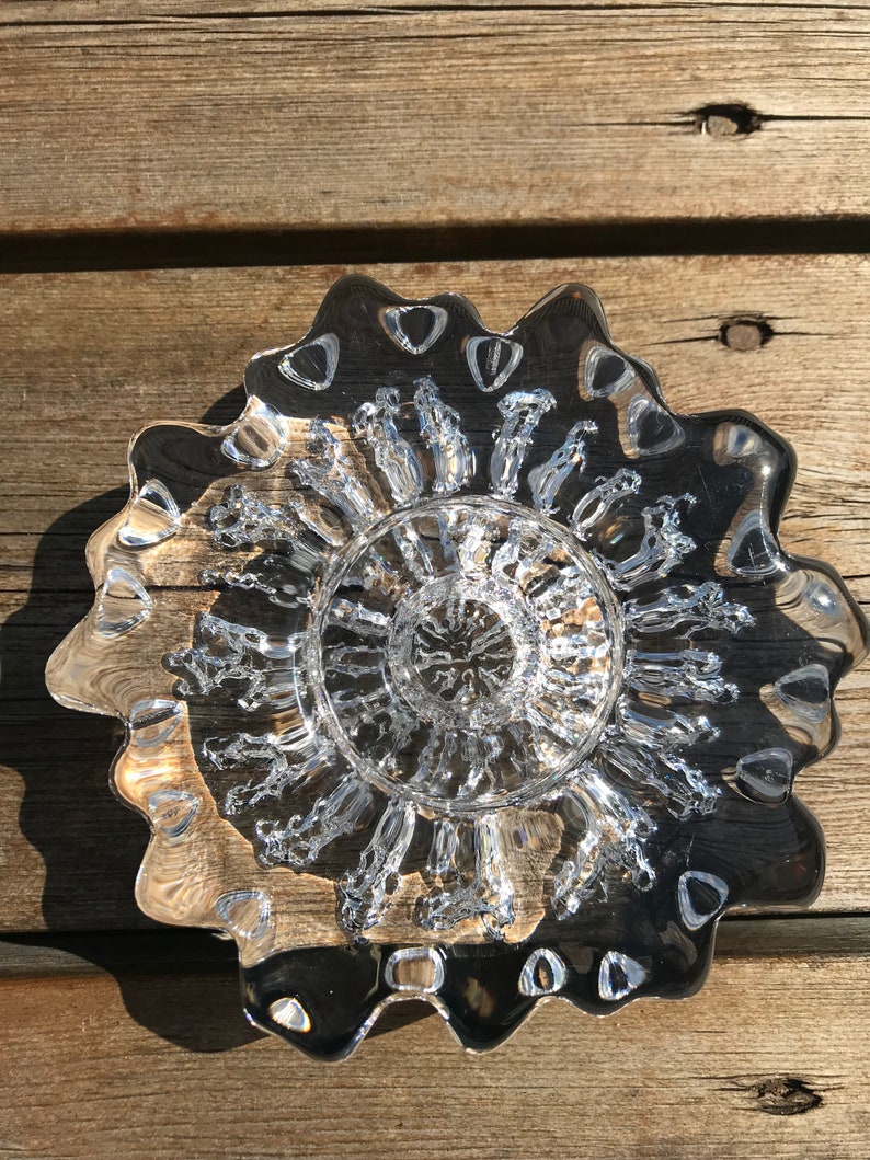 Pu&ograve; includere: Un piatto di vetro trasparente con un bordo ondulato e un design testurizzato a forma di bolle al centro.