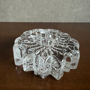 Pu&ograve; includere: Un portacandele in vetro trasparente con un design a forma di stella. Il portacandele ha un centro rialzato per una candela e una superficie testurizzata e sfaccettata.