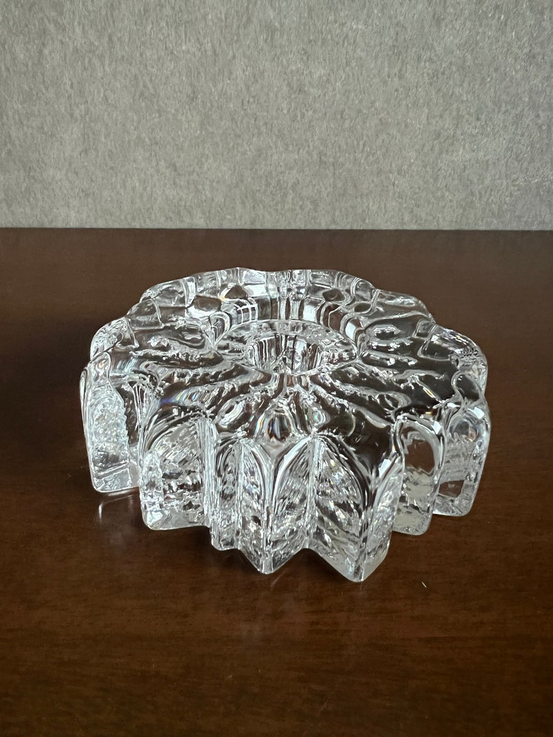 Pu&ograve; includere: Un portacandele in vetro trasparente con un design a forma di stella. Il portacandele ha un centro rialzato per una candela e una superficie testurizzata e sfaccettata.