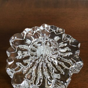 Pu&ograve; includere: Un portacandele in vetro trasparente con un design a stella. Il portacandele ha una superficie testurizzata e una base rotonda.