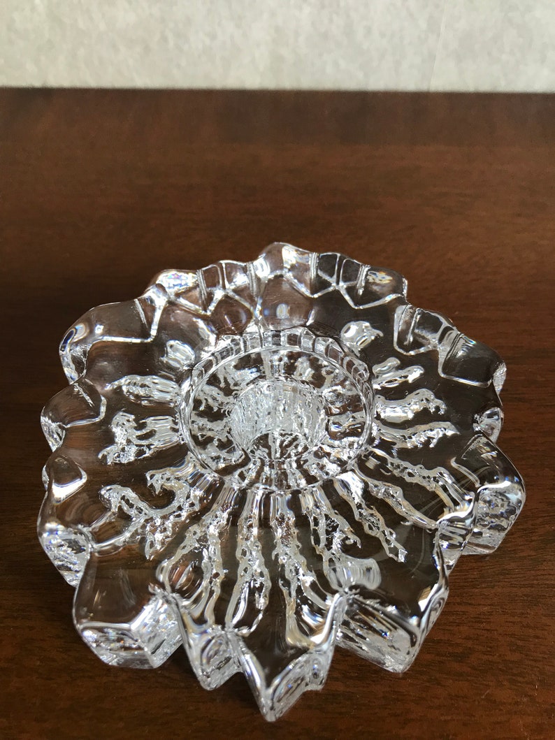 Pu&ograve; includere: Un portacandele in vetro trasparente con un design a stella. Il portacandele ha una superficie testurizzata e una base rotonda.