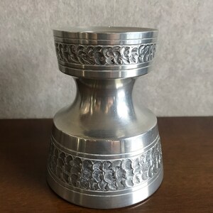 May include: A silver metal vase with an ornate design. The vase has a wide base and a narrow neck.