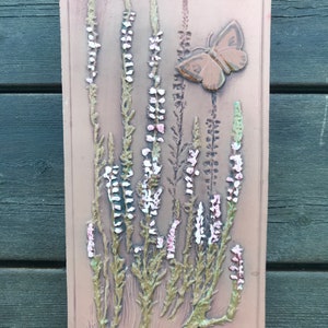 May include: A brown ceramic wall plaque with a raised design of pink and white flowers and a brown butterfly. The plaque has a brown background and a brown border. The plaque is signed "jic" in the lower left corner.