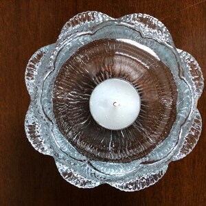 May include: A clear glass candle holder with a textured, wavy design. The holder has a round, open top and a single, white tea light candle inside.