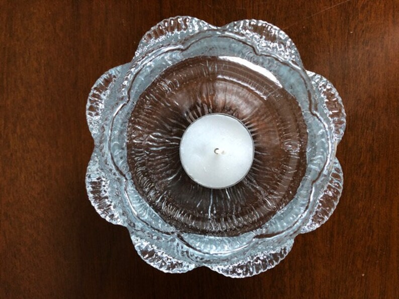 May include: A clear glass candle holder with a textured, wavy design. The holder has a round, open top and a single, white tea light candle inside.