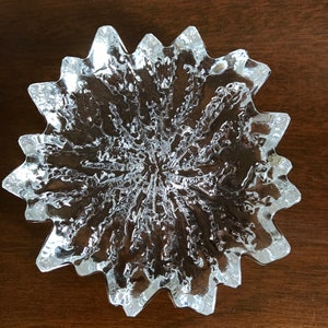 Pu&ograve; includere: Un piatto di vetro trasparente con un design a stella. Il piatto ha una superficie testurizzata e un bordo smerlato.