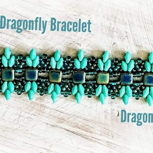 Può includere: Un braccialetto di perline turchesi e nere con una chiusura a forma di cuore. Il braccialetto presenta un motivo geometrico ed è etichettato "Dragonfly Bracelet" e "Dragonfly Designs".