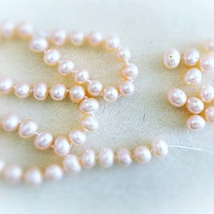 Könnte beinhalten: Eine weiße Perlenkette mit einer kleineren Perlenkette an der Seite. Die Perlen sind in einem lockeren, fließenden Muster angeordnet.