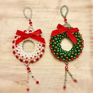 Puede incluir: Dos coronas de Navidad de cuentas con lazos rojos. Una corona es blanca y la otra es verde.