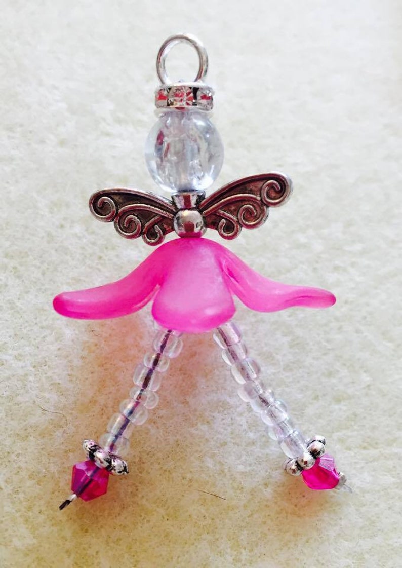 May include: A pink beaded angel charm with clear glass beads and silver wings. The angel has a pink head and a silver loop at the top for hanging.