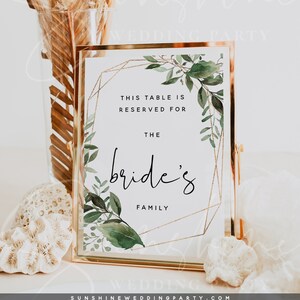 May include: A gold-framed table sign with a white background and green watercolor leaves. The sign reads "This table is reserved for the bride's family".