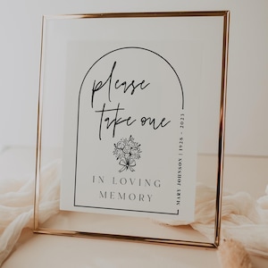 Könnte beinhalten: Ein gerahmtes Schild mit einem goldfarbenen Metallrahmen. Das weiße Papier im Inneren trägt den schwarzen Text "Please take one" über einer floralen Illustration und "In Loving Memory". Das Schild enthält auch den Namen und die Daten "Mary Johnson | 1928 - 2023".