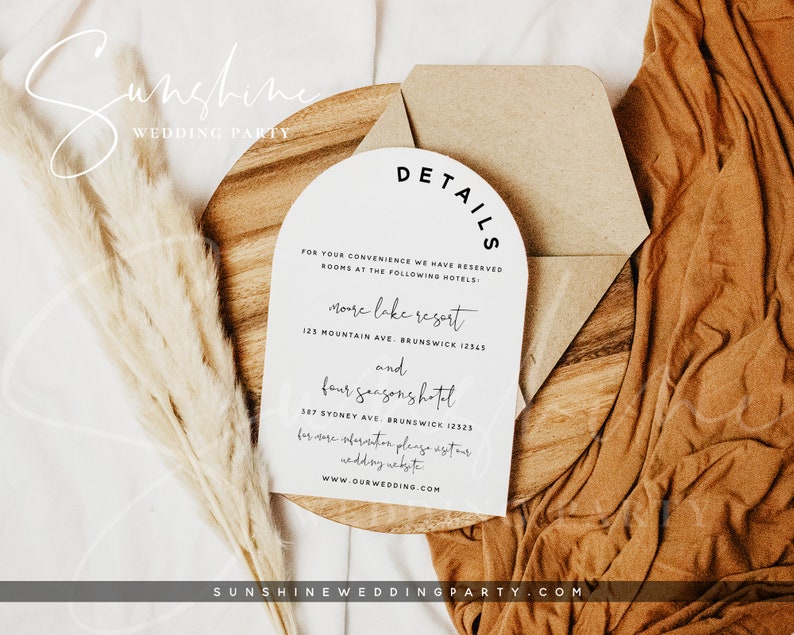 Op de afbeelding: Een witte kaart met zwarte tekst op een houten oppervlak. De kaart heeft de tekst "DETAILS" in een gebogen lettertype. De tekst op de kaart vermeldt twee hotels: "More Lake Resort" en "Four Seasons Hotel" met hun adressen. De kaart bevat ook de website "www.ourwedding.com".