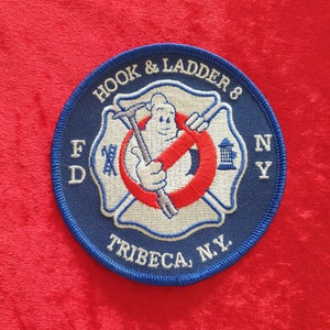 May include: Blue and white embroidered patch with a red circle and a fireman holding a hook and ladder. The patch says "Hook & Ladder 8 FDNY Tribeca, N.Y."