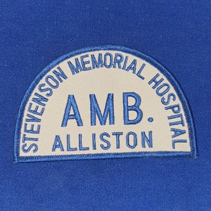 Op de afbeelding: Een blauw en wit geborduurd patch met de tekst "Stevenson Memorial Hospital" en "AMB. Alliston" in een cirkelvorm.