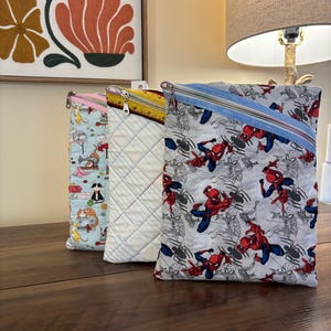 May include: Three quilted zipper pouches with different patterns. One has a light blue background with cats and sewing machines, another has a lined paper design, and the third features a Spider-Man print.