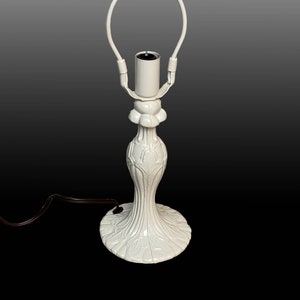 May include: White ceramic table lamp with a decorative floral design. The lamp has a simple, elegant design and a white cord.