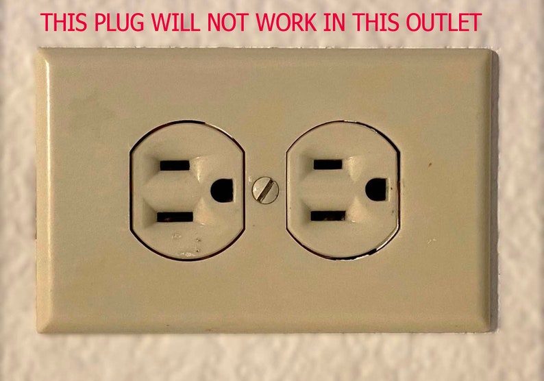 Op de afbeelding: Een close-up van een beige stopcontact met twee standaard stopcontacten met drie pinnen. De tekst "THIS PLUG WILL NOT WORK IN THIS OUTLET" staat boven het stopcontact.