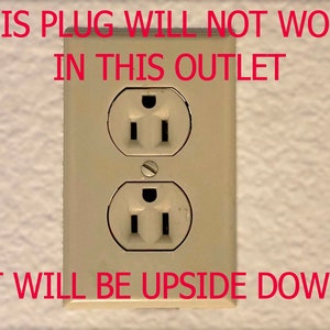 Op de afbeelding: Een close-up van een standaard stopcontact met de tekst "THIS PLUG WILL NOT WORK IN THIS OUTLET IT WILL BE UPSIDE DOWN" erboven.