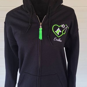 May include: Black zip-up hoodie with a green embroidered heart, a dog silhouette, a stethoscope, and the name "Erika" on the front.