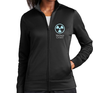 May include: Black zip-up jacket with a light blue radiation symbol and the text "Melissa CNMT" on the upper left chest. The jacket has a high collar, two front pockets, and a full-length zipper.