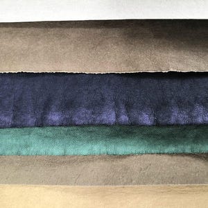 May include: A stack of six different colored leather swatches. The swatches are arranged from top to bottom: white, brown, dark blue, green, light brown, and black.