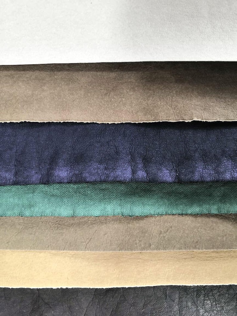 May include: A stack of six different colored leather swatches. The swatches are arranged from top to bottom: white, brown, dark blue, green, light brown, and black.