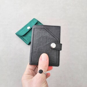 May include: Two small wallets, one black and one green, with a snap closure. The black wallet has a flap with a silver button.
