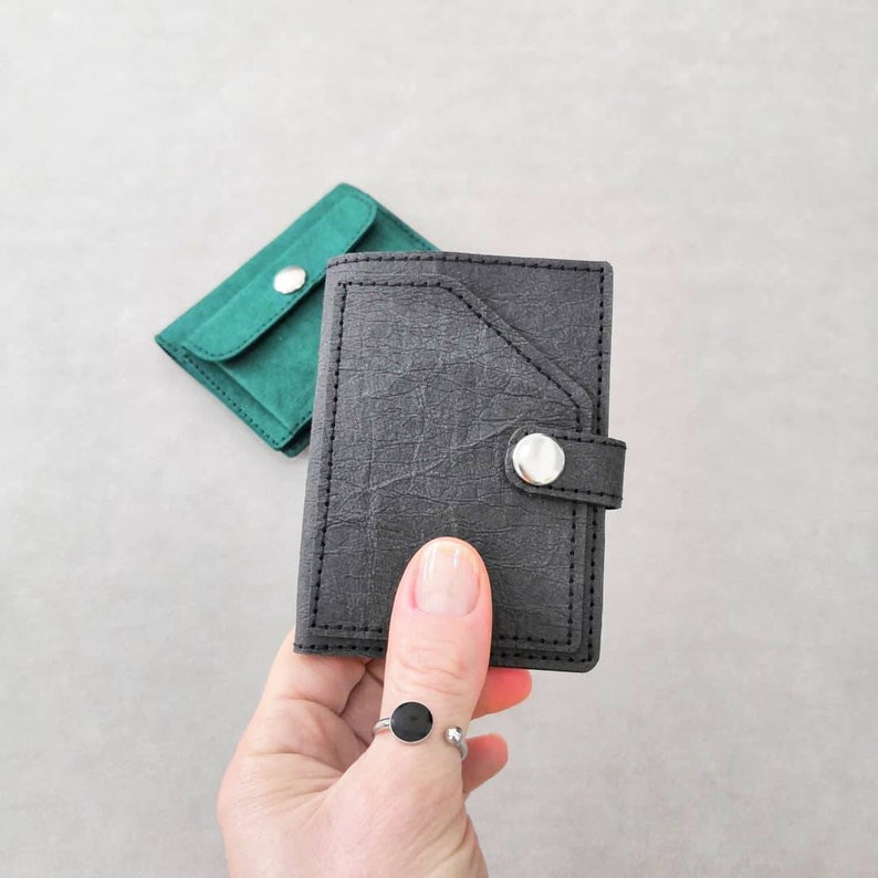 May include: Two small wallets, one black and one green, with a snap closure. The black wallet has a flap with a silver button.